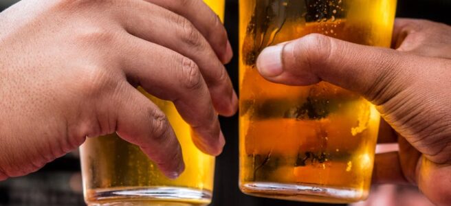two persons holding drinking glasses filled with beer